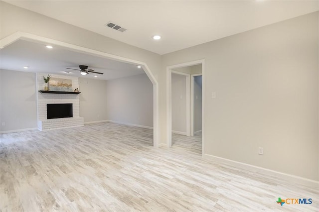 unfurnished living room with a brick fireplace, ceiling fan, and light wood-type flooring