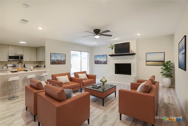 living room featuring a fireplace, light hardwood / wood-style flooring, and ceiling fan