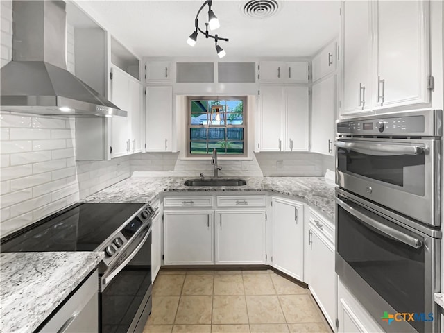 kitchen featuring stainless steel appliances, wall chimney exhaust hood, sink, tasteful backsplash, and white cabinetry