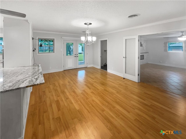 unfurnished dining area featuring french doors, a chandelier, a textured ceiling, crown molding, and light hardwood / wood-style flooring