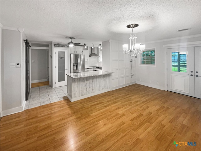 kitchen with stainless steel appliances, light hardwood / wood-style floors, wall chimney exhaust hood, and decorative light fixtures