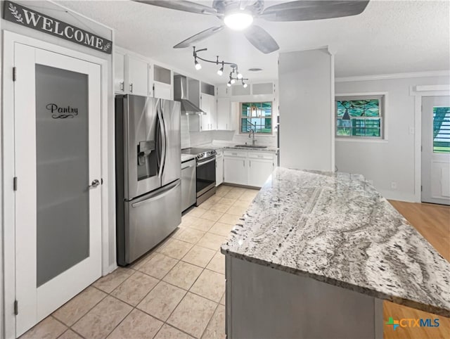 kitchen with light stone counters, wall chimney exhaust hood, sink, white cabinetry, and appliances with stainless steel finishes