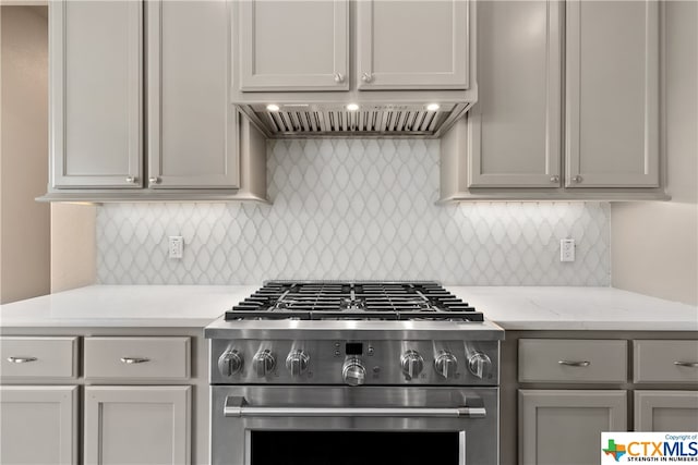 kitchen featuring tasteful backsplash, light stone countertops, gray cabinets, stainless steel stove, and premium range hood