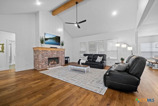 living room with wood-type flooring, high vaulted ceiling, a brick fireplace, ceiling fan, and beam ceiling