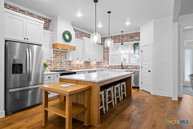 kitchen featuring a kitchen island, brick wall, appliances with stainless steel finishes, decorative light fixtures, and white cabinets