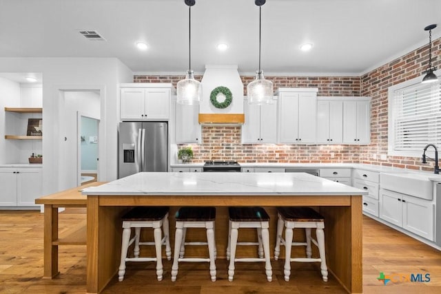 kitchen featuring stainless steel appliances, hanging light fixtures, a center island, and white cabinets