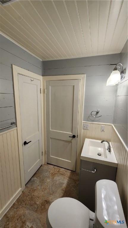 bathroom featuring wood walls, vanity, wooden ceiling, and toilet