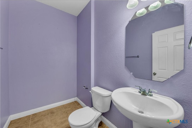 half bath with tile patterned flooring, toilet, baseboards, and a sink