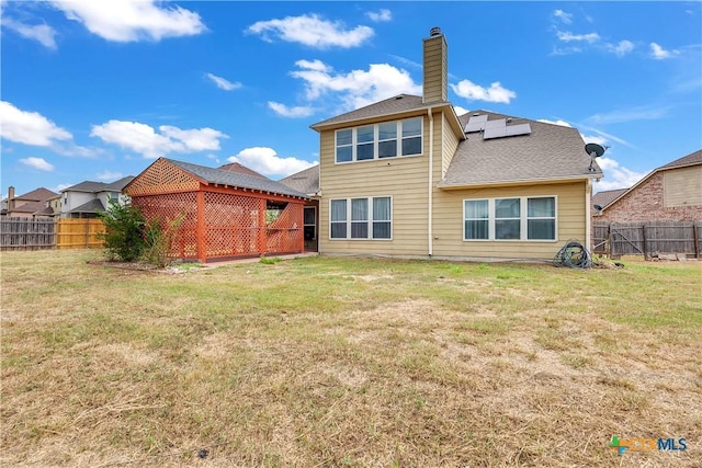 back of property with solar panels, a yard, and a fenced backyard