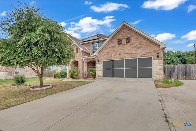 view of front of house featuring fence, concrete driveway, stone siding, brick siding, and roof mounted solar panels