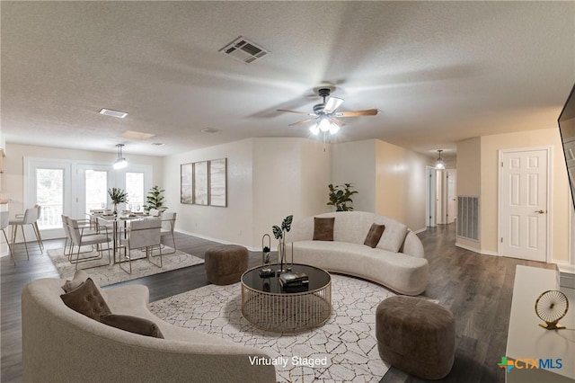 living room featuring baseboards, a textured ceiling, visible vents, and dark wood-type flooring