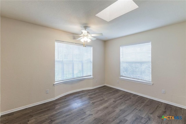 spare room with ceiling fan, a skylight, dark wood finished floors, and baseboards