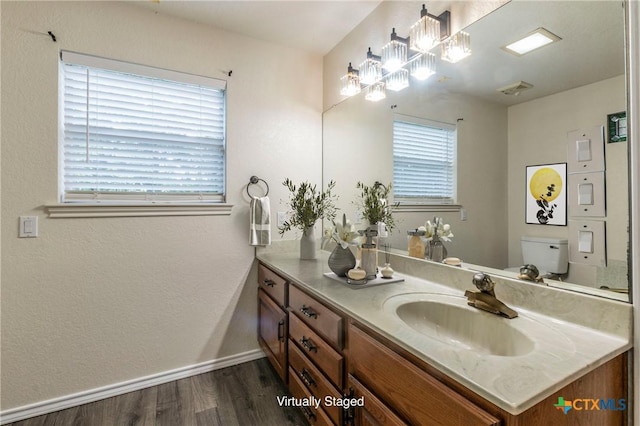 bathroom with toilet, plenty of natural light, wood finished floors, and vanity