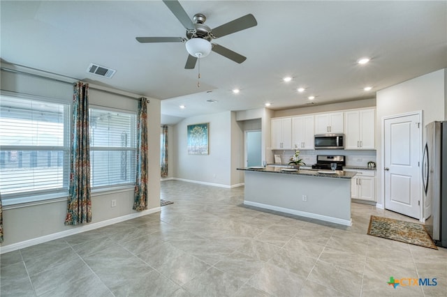 kitchen featuring dark stone counters, ceiling fan, an island with sink, white cabinetry, and stainless steel appliances