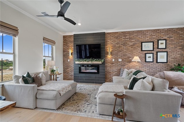 living room with brick wall, a glass covered fireplace, a ceiling fan, wood finished floors, and ornamental molding