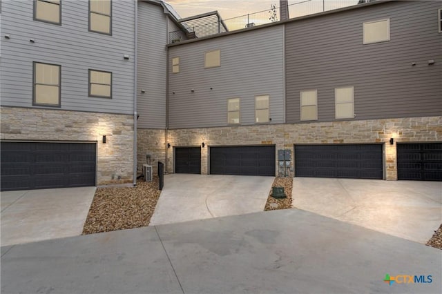 exterior space with an attached garage, cooling unit, driveway, and stone siding