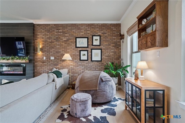 living area featuring brick wall, a glass covered fireplace, ornamental molding, and light wood-type flooring
