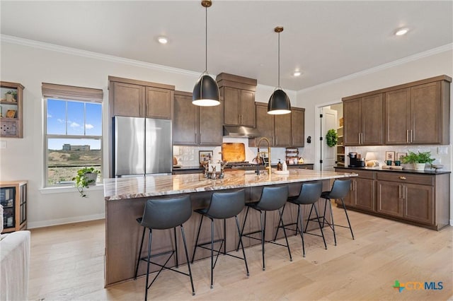 kitchen with freestanding refrigerator, decorative backsplash, light wood-type flooring, under cabinet range hood, and light stone counters