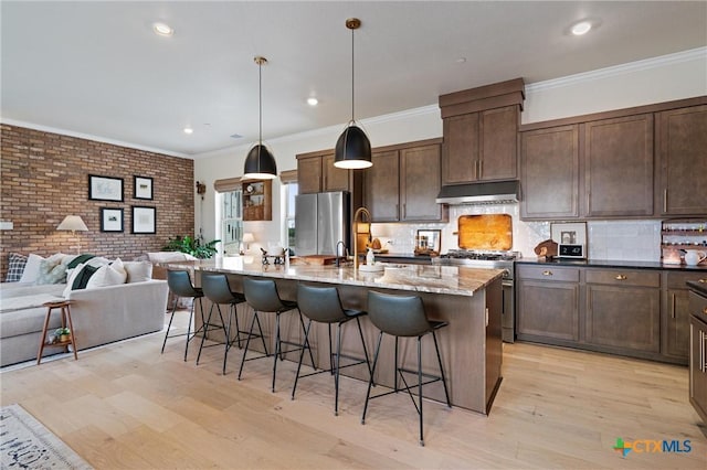kitchen with open floor plan, a breakfast bar area, under cabinet range hood, light wood finished floors, and stainless steel appliances