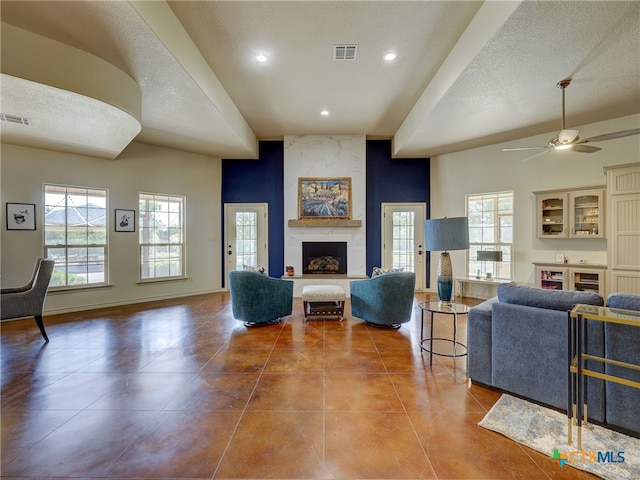 tiled living room featuring ceiling fan, plenty of natural light, a large fireplace, and a textured ceiling