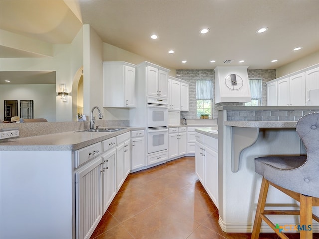 kitchen with light tile patterned flooring, a breakfast bar area, white cabinetry, and white double oven