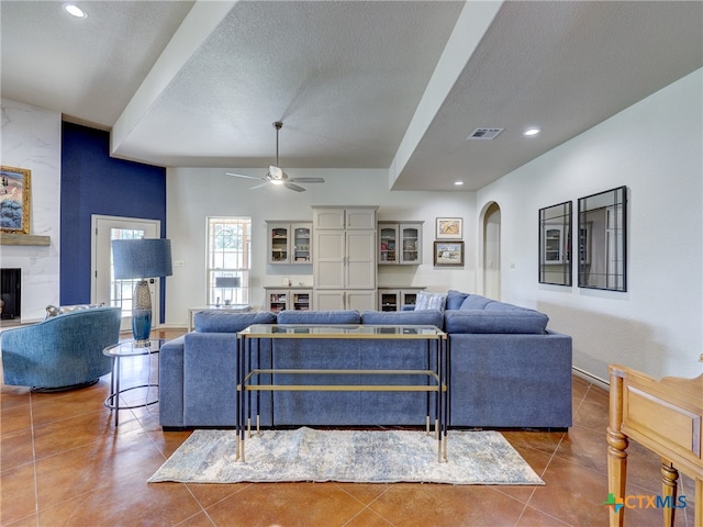 tiled living room with a textured ceiling, a large fireplace, and ceiling fan