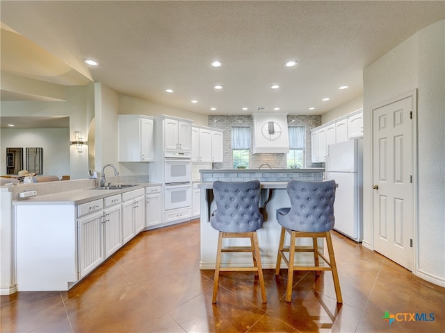 kitchen with light tile patterned flooring, white cabinetry, sink, kitchen peninsula, and white appliances