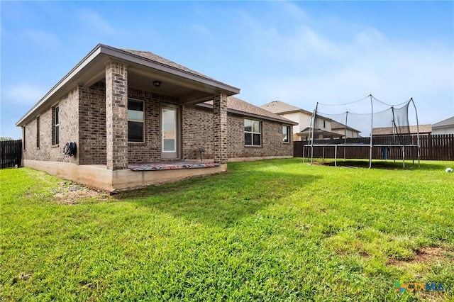 back of house featuring brick siding, a trampoline, and a patio