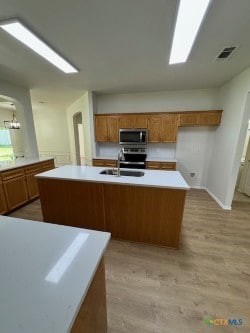 500 Chickasaw Dr, Harker Heights, TX 76548 - kitchen with stainless steel appliances, brown cabinets, light countertops, a kitchen island with sink, and light wood-style floors