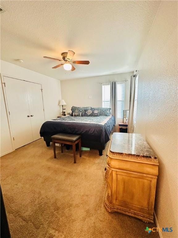 bedroom with a textured ceiling, ceiling fan, a closet, and light colored carpet