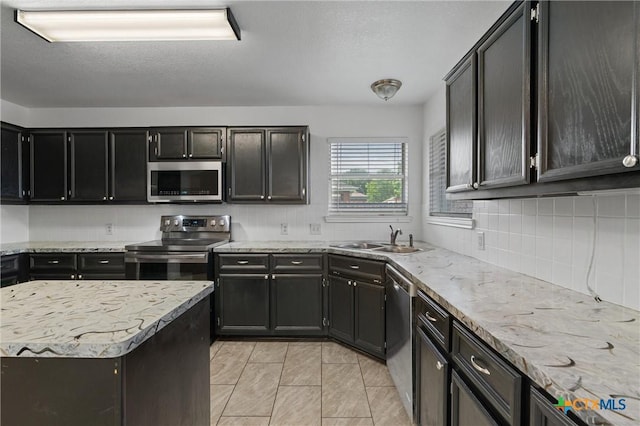 4401 Maggie Dr, Killeen, TX 76549 - kitchen featuring stainless steel appliances, a sink, tasteful backsplash, dark cabinets, and light stone counters