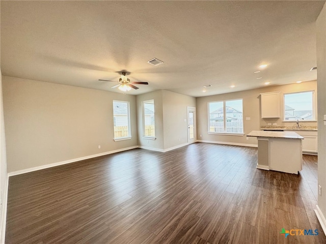 unfurnished living room featuring dark wood-type flooring, ceiling fan, sink, and a textured ceiling