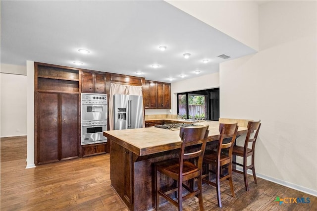105 Creekside Dr, Victoria, TX 77904 - kitchen featuring stainless steel appliances, butcher block countertops, a peninsula, dark brown cabinets, and wood finished floors