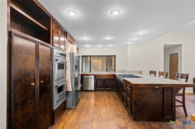 105 Creekside Dr, Victoria, TX 77904 - kitchen with stainless steel appliances, a kitchen bar, dark brown cabinetry, light countertops, and dark wood finished floors
