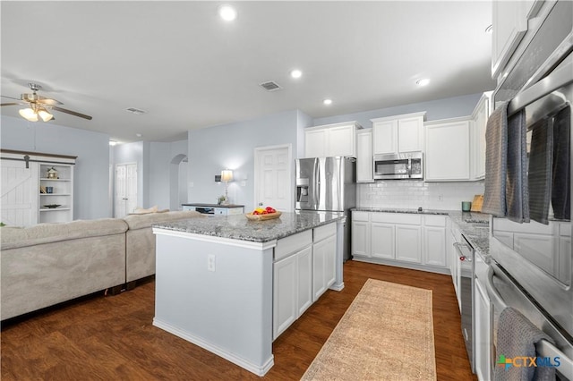 kitchen featuring arched walkways, stainless steel appliances, a center island, backsplash, and light stone countertops