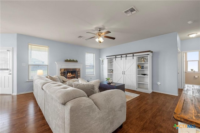 living room featuring a wealth of natural light, a barn door, visible vents, and dark wood-style flooring