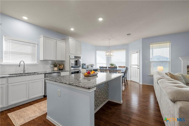 kitchen with tasteful backsplash, dark wood finished floors, a kitchen island, double oven, and a sink