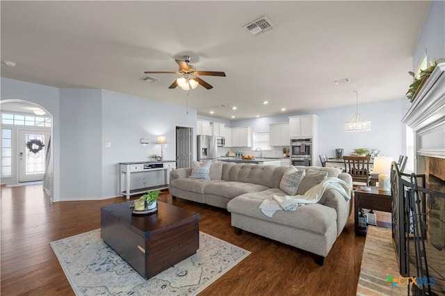 living room with dark wood-style floors, a fireplace, visible vents, and arched walkways