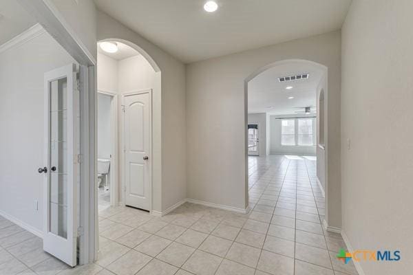 hall with arched walkways, visible vents, baseboards, and light tile patterned floors