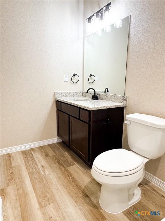 half bath featuring toilet, vanity, baseboards, and wood finished floors