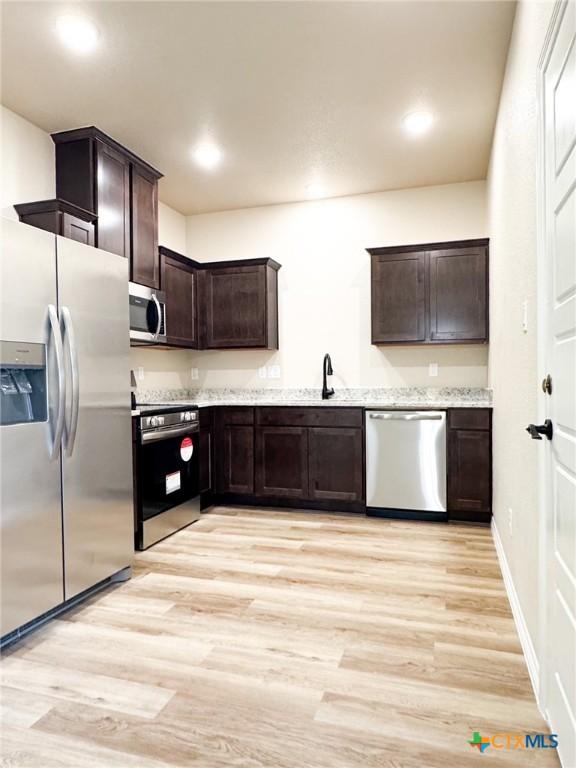 kitchen featuring a sink, stainless steel appliances, light wood finished floors, light stone countertops, and dark brown cabinets