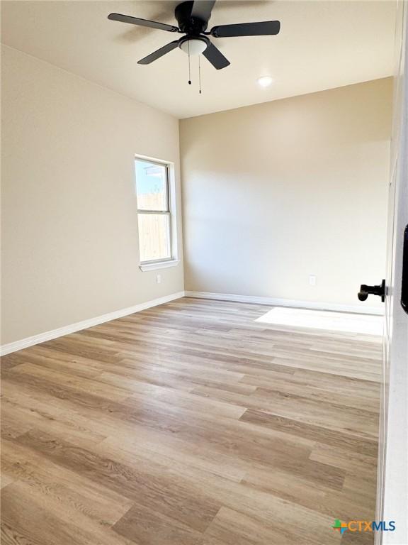 spare room featuring baseboards, light wood-style floors, and a ceiling fan