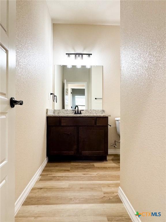 half bathroom featuring vanity, toilet, wood finished floors, and baseboards