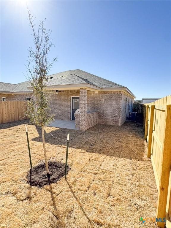 rear view of house featuring brick siding, a patio, central AC, and a fenced backyard