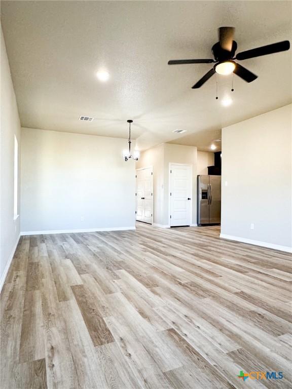 unfurnished living room featuring ceiling fan with notable chandelier, light wood-style flooring, baseboards, and visible vents