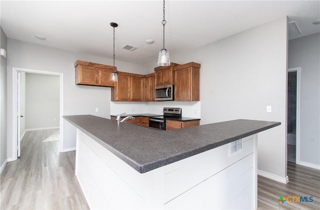 kitchen with sink, appliances with stainless steel finishes, hardwood / wood-style floors, pendant lighting, and a kitchen island with sink