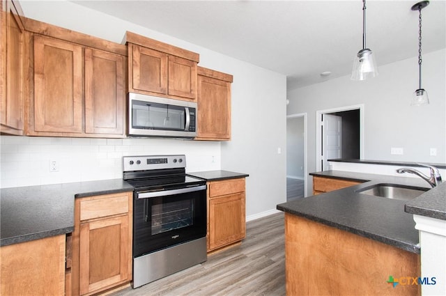 kitchen with dark wood-type flooring, sink, tasteful backsplash, hanging light fixtures, and stainless steel appliances