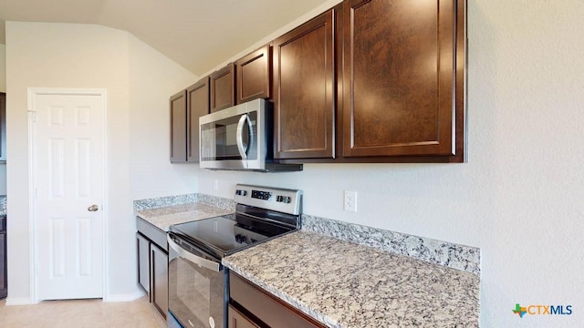 kitchen featuring light stone counters, dark brown cabinets, vaulted ceiling, and stainless steel appliances