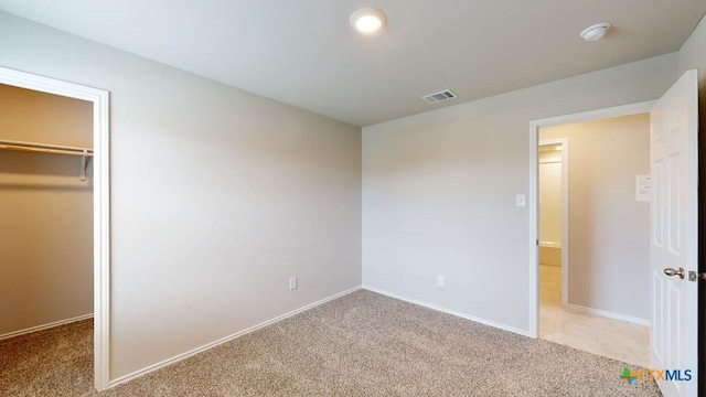 unfurnished bedroom featuring a spacious closet, light colored carpet, and a closet