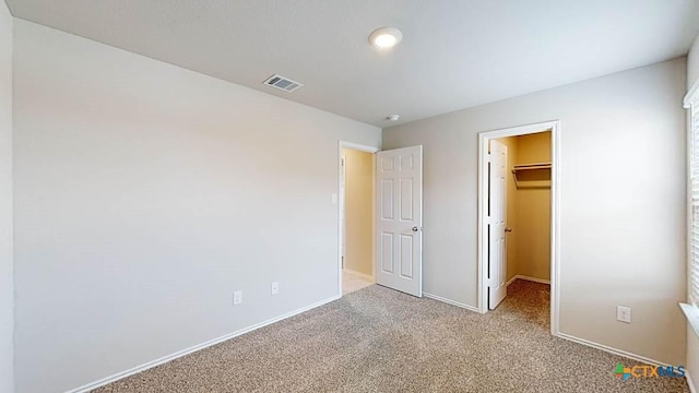 unfurnished bedroom with a walk in closet, a closet, and carpet flooring